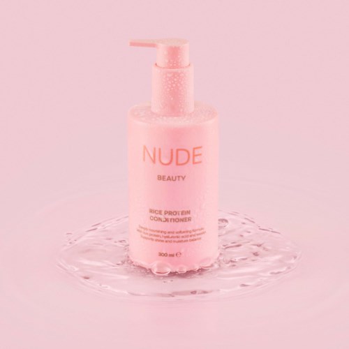 Roze fles met NUDE BEAUTY op water rond het op roze achtergrond.