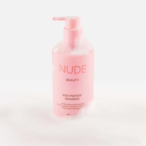 Roze fles met NUDE Beauty Rice Protein Shampoo met pomp, ziet er schoon en eenvoudig uit.