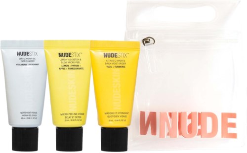 Drei gelbe und weiße Hautpflege-Tuben mit NUDE STIX und eine transparente Tasche mit rosa NUDE-Text.