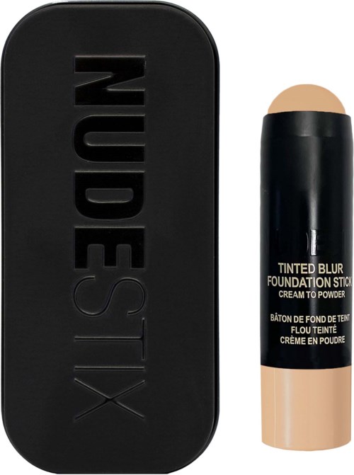 Ein schwarzer kompaktes Etui mit dem Wort 'NUDESTIX' geprägt, neben einem beigefarbenen Stick-Foundation mit schwarzem Deckel.
