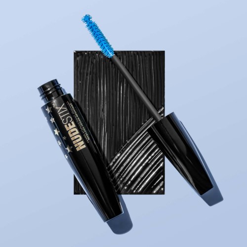 Eine schwarze Mascara-Hülse mit weißen Sternen, blauer Mascara-Bürste und schwarzem strukturiertem Hintergrund.