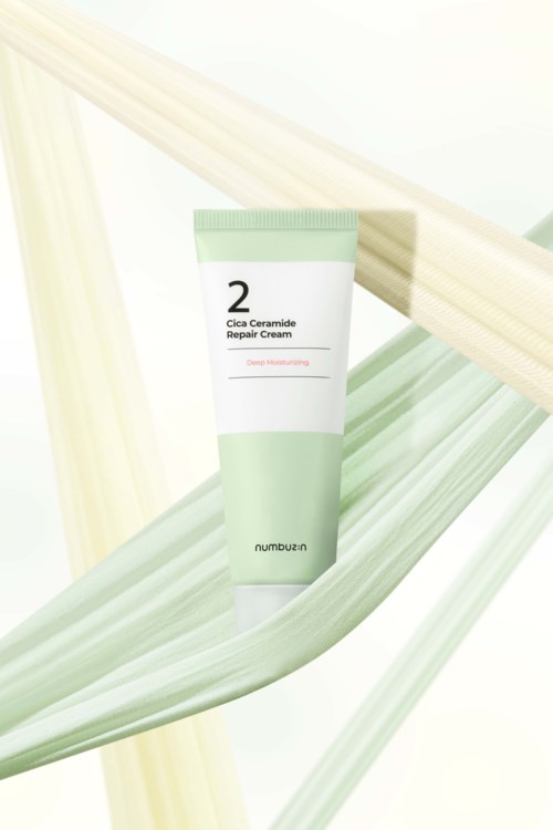A tube of skincare cream, labeled 'Cica Ceramide Repair Cream,' with green and white packaging, surrounded by green leaves.