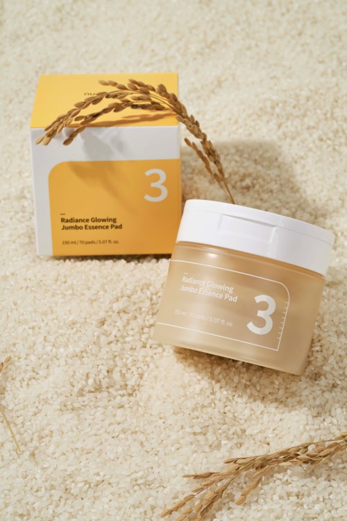 Een pot en doos van huidverzorgingsproduct met label 'Radiance Glowing' met nummer 3, op een beige pluizige ondergrond.