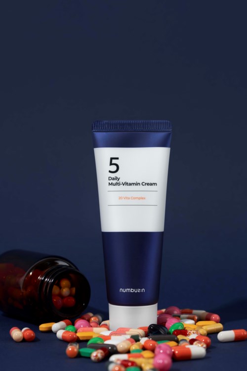 En tube merket 'Daily Multi-Vitamin Cream' står oppreist, med en brunsflaske som er trukket over og sølte piller.