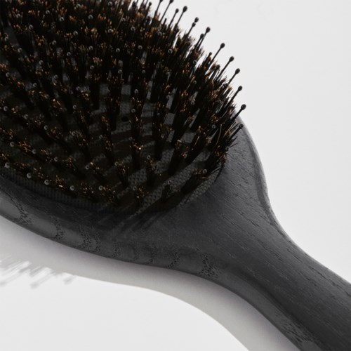 Eine schwarze Haarbürste mit rundem Kopf und Borsten. Sie liegt auf einer hellen, flachen Oberfläche.