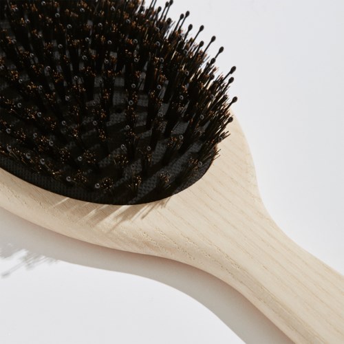 Een houten haarborstel met zwarte borstelharen. De borstel heeft een ronde handgreep en is tegen een witte achtergrond gefotografeerd.