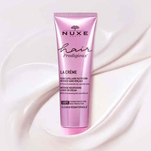 Rod rosa tub med NUXE hår närande kräm på vit sammetslen tyg, med svart och rosa text, och lock upptill.