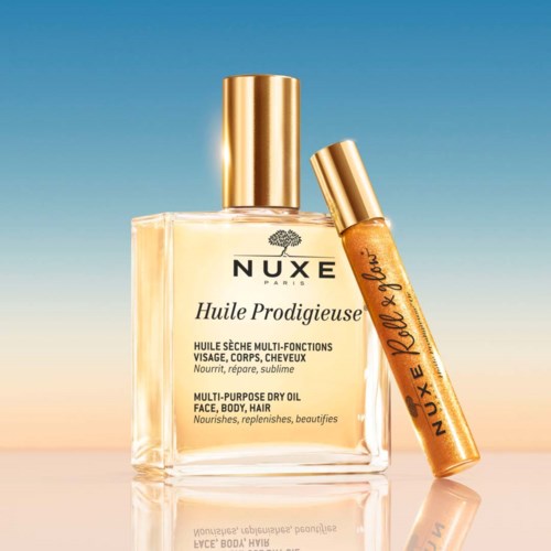 A bottle of Nuxe dry oil for face and body, with a gold cap, and a small roller tube beside it.