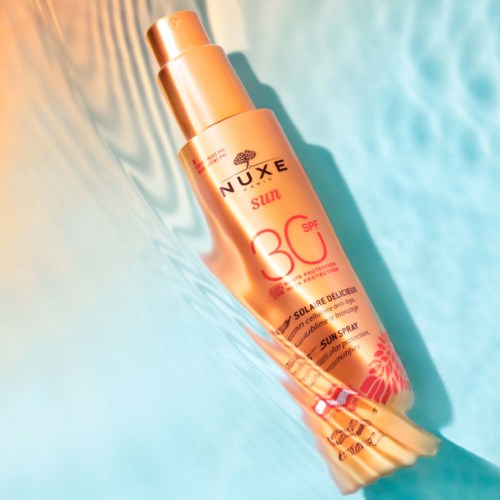 En solkremflaske merket 'NUXE Sun SPF 30' på en fargerik, abstrakt bakgrunn med blå og oransje nyanser.