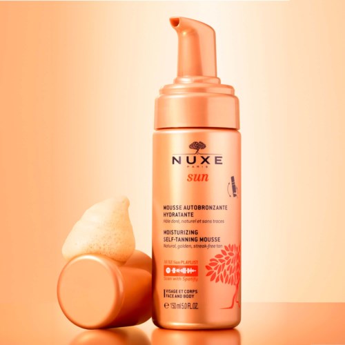 En flaska Nuxe Sun mineralsmousse med orange pump, bredvid en skum applicator.