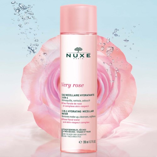 En lång rosa flaska med Nuxe Very Rose hydrerande micellarvatten mot en bakgrund med en rosa ros och vattendroppar.