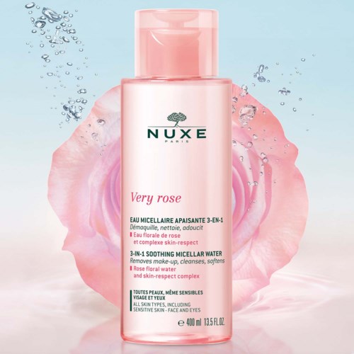 A pink bottle of NUXE Very Rose Korean micellar water with pink rose petals around it, outdoors.