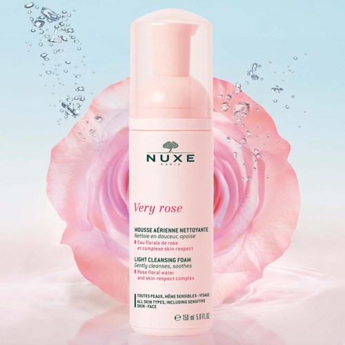 Rosa flaska av NUXE Very Rose rengöringsskum med en rosblomma och vattendroppar i bakgrunden.