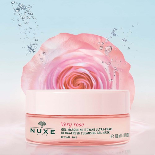 En rosa ros bakom en burk av NUXE Vera Rose rengöringsgel, med bubblor och ljusblå bakgrund.