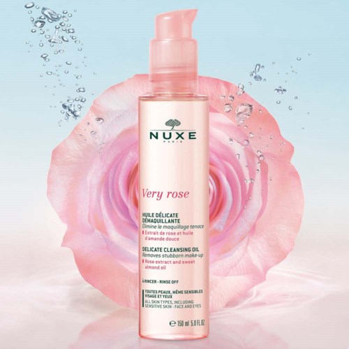 En rosa flaska med Nuxe Very Rose rengöringsolja, med en ros bakom, vattendroppar runtom och text på flaskan.