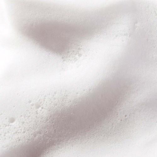Skummig vit yta med små bubblor och mjuka kurvor, liknar tvålfog eller skummande vätska.
