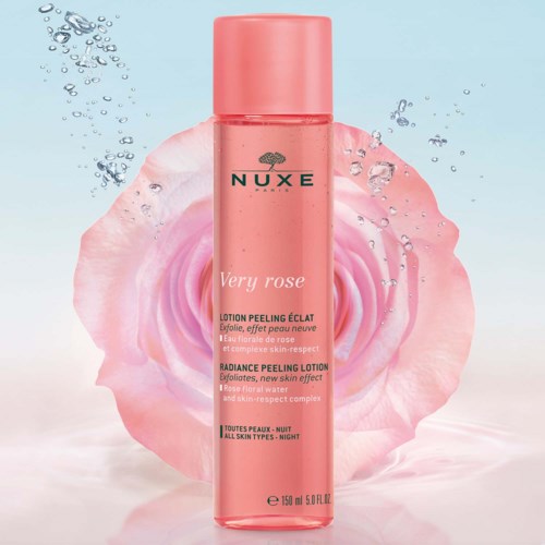 En rosa flaska från Nuxe Very Rose Radiance Peeling Lotion framför en rosa rosenblomma med vatten droplets runt.