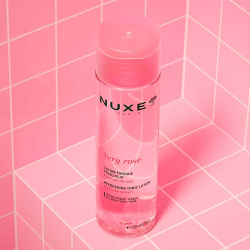 En rosa flaska med Nuxe hudvårdslotion med rosa lock, står på en rosa kaklad yta.