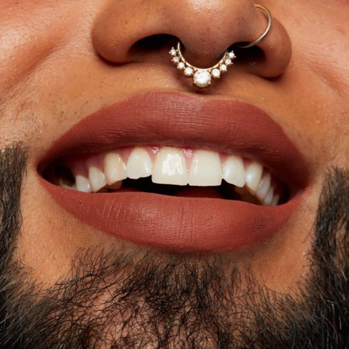 Lask bilde av en person med en nese piercing og et åpent smil som viser tenner og leppemaling.