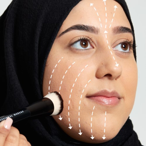 A woman applies makeup on her cheek with a brush, with white lines indicating facial contouring directions.