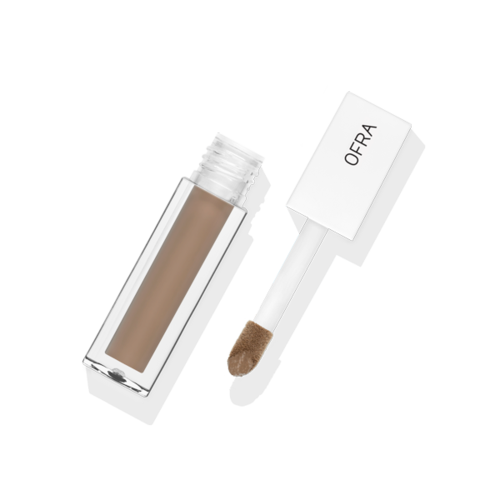 En liten borste med vit handtag märkt 'OFRA' och en genomskinlig behållare med beige smink.
