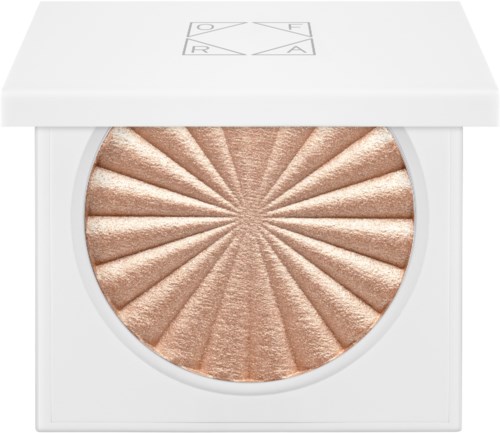 En skinnende beige highlighter med et solstrålermønster i en hvit emballasje. Låsen har en logo med bokstaver og en stjerne.