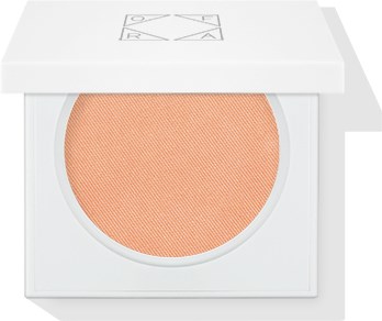 En makeup blush-emballage med ferskenfarvet pudder indeni og et hvidt etui.