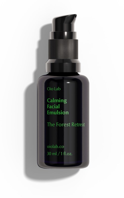 En svart flaska med pump, märkt 'Calming Facial Emulsion' för hudvård, med grön text och produktenamn.