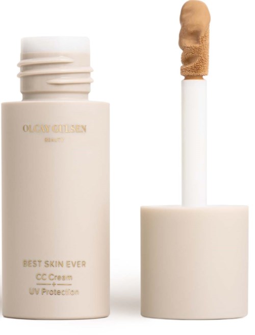 En beige flaska med CC-kräm, vit lock och en borste med brunt innehåll. Flaskan har guldtext.