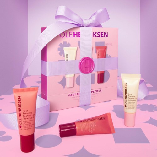 A pink gift box with a purple ribbon, containing skincare products, set against a pink background with decorative shadows.