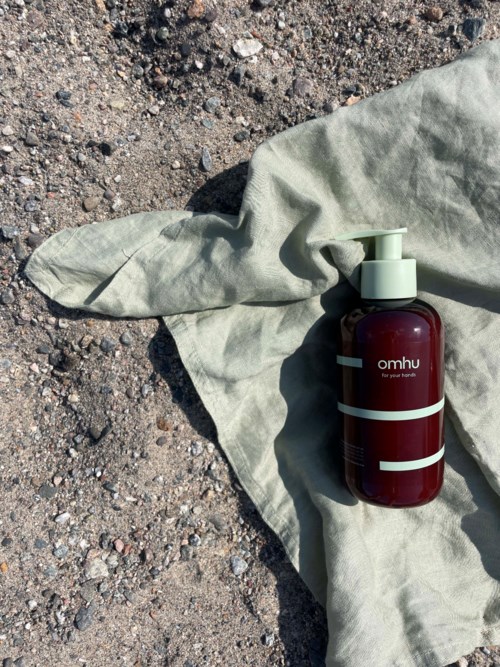 En röd flaska med pump på ett ljust tygstycke på marken utomhus.