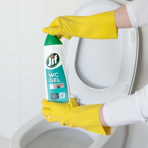En person med gule hansker holder en sprayflaske nær en ren toalett.
