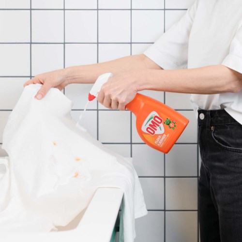 Eine Person sprüht Reinigungsmittel auf ein weißes Tuch in einem Wäschebereich.