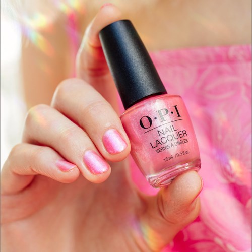 En hand håller en rosa nagellackflaska med svart lock, visar målade naglar som matchar nagellacket.