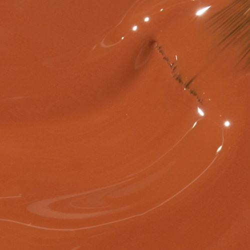 A close-up of a droplet in orange liquid with light reflections and a palm leaf at the edge.