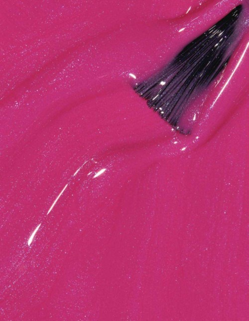 En sminkborste breder ut glänkande rosa nagellack. Nagellacket glittrar med glitter.