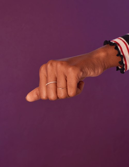 En hand med ringar som pekar åt vänster, iklädd randig klädsel och mot en lila bakgrund.