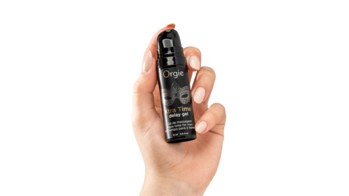 En hånd holder en liten svart sprayflaske merket "Orgie Ultra Time Delay Gel" med pumpe.