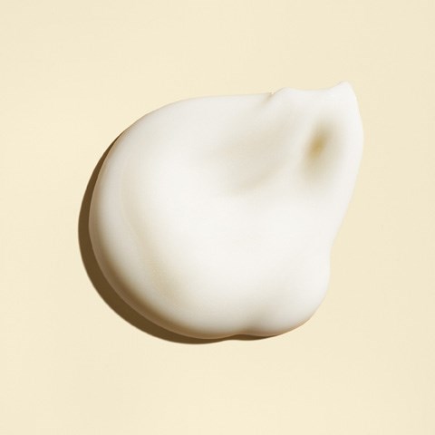 En klatt hvit krem eller lotion på en lys bakgrunn med myke skygger.