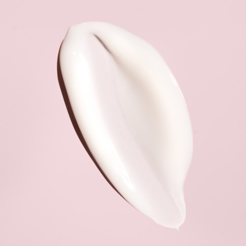 En vit kräm eller lotion på en ljusrosa bakgrund, formad i en slät, förlängd form.