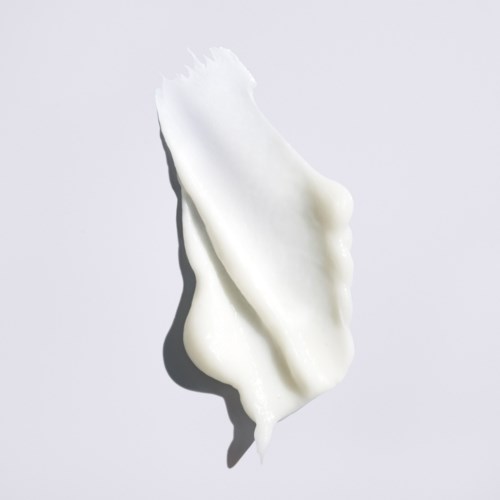 En klump med hvit krem eller lotion med ujevn, teksturert overflate på en enkel bakgrunn.