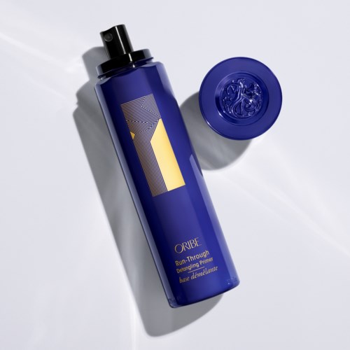 A blue bottle with a black cap and a matching blue lid, labeled 'Oribe', stands on white background.