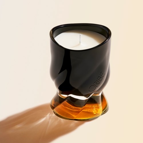 En svart og amber farget glasslysestake med et hvitt lys inni, som kaster skygge på overflaten.