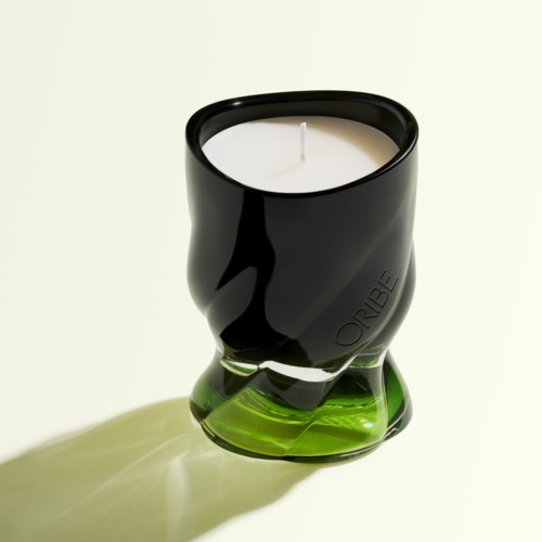 A black and green candle holder with a white candle inside, casting a shadow on a light background.