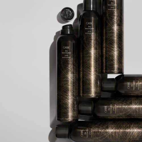 Six black bottles with gold lines and labels are arranged on a white surface.