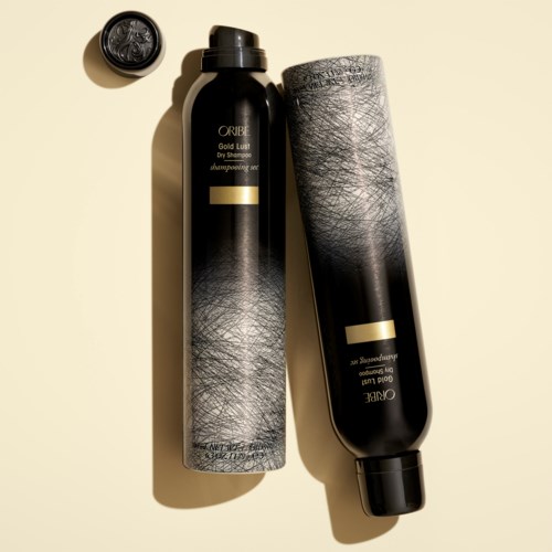 Två svarta flaskor av Oribe-shampon ligger på en beige yta, med ett litet lock och tillhörande etikett.