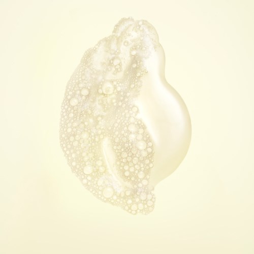 Een beige, schuimige vloeistof vormt een klomp met veel bellen en schuim op een lichte achtergrond.