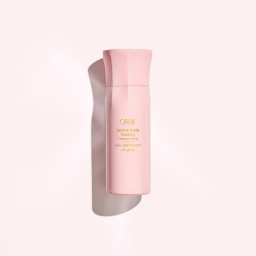 En rosa flaska märkt 'Oribe Serene Scalp Thickening Treatment Spray' står upprätt med en skugga på en ljus bakgrund.