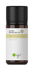 Liten flaska märkt 'Camellia Essential Hair Oil' med svart lock och grönvit etikett.