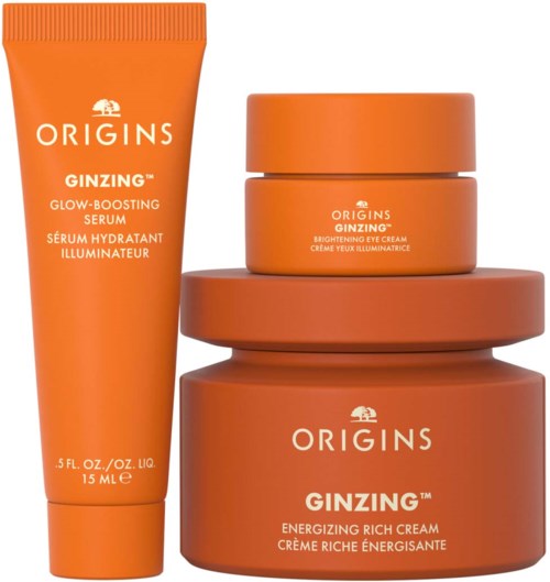 Et sett med hudpleieprodukter i oransje beholdere, inkludert en tube, en liten krukke og to større krukker. Teksten sier Origins Ginzing.